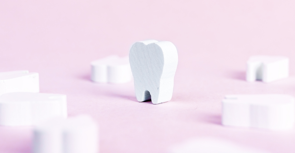 White tooth made of wood on a pink background.