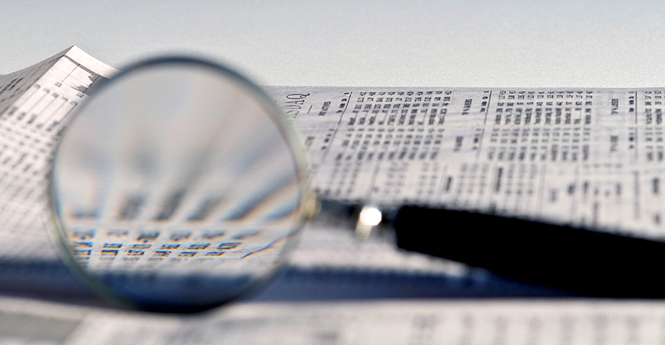A magnifying glass lying on a newspaper showing financial numbers