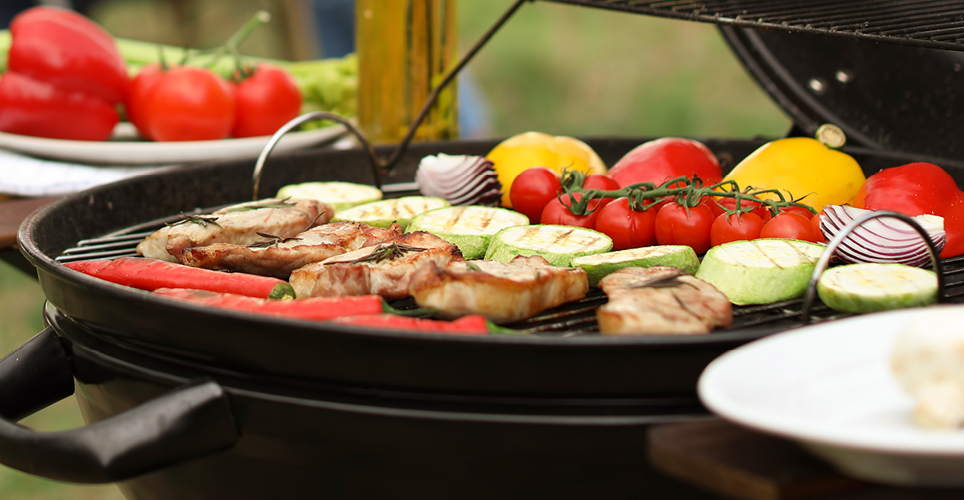 an outdoor grill with fresh vegetables and meat cooking