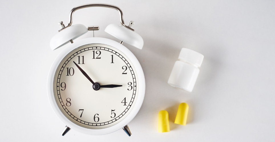 White clock with pill bottle and ear plugs to the right of it. 