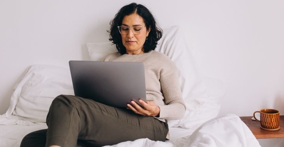Woman sitting on bed with laptop sitting on her lap.