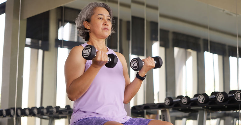 Asian woman lifting free weights with both arms.